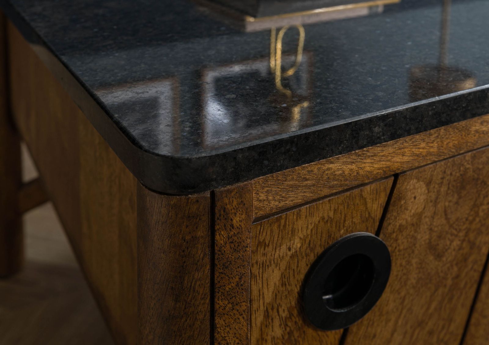 Rund geschliffene Kante eines Möbelstücks mit schwarzer Granit-Platte. Dekorative Objekte spiegeln sich edel auf der schimmernden Oberfläche, zudem entsteht ein attraktiver Kontrast zum Holz.